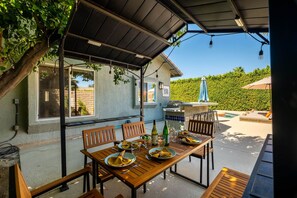 An outdoor dining area with a table set for two, a grill, and a poolside lounge with umbrellas. - Cool Pool/Spa Retreat near Shops & Surf Club (Palm Springs)