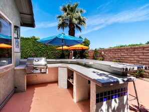 An outdoor barbecue area with a grill, a built-in table, and umbrellas providing shade. - Cool Pool/Spa Retreat near Shops & Surf Club (Palm Springs)