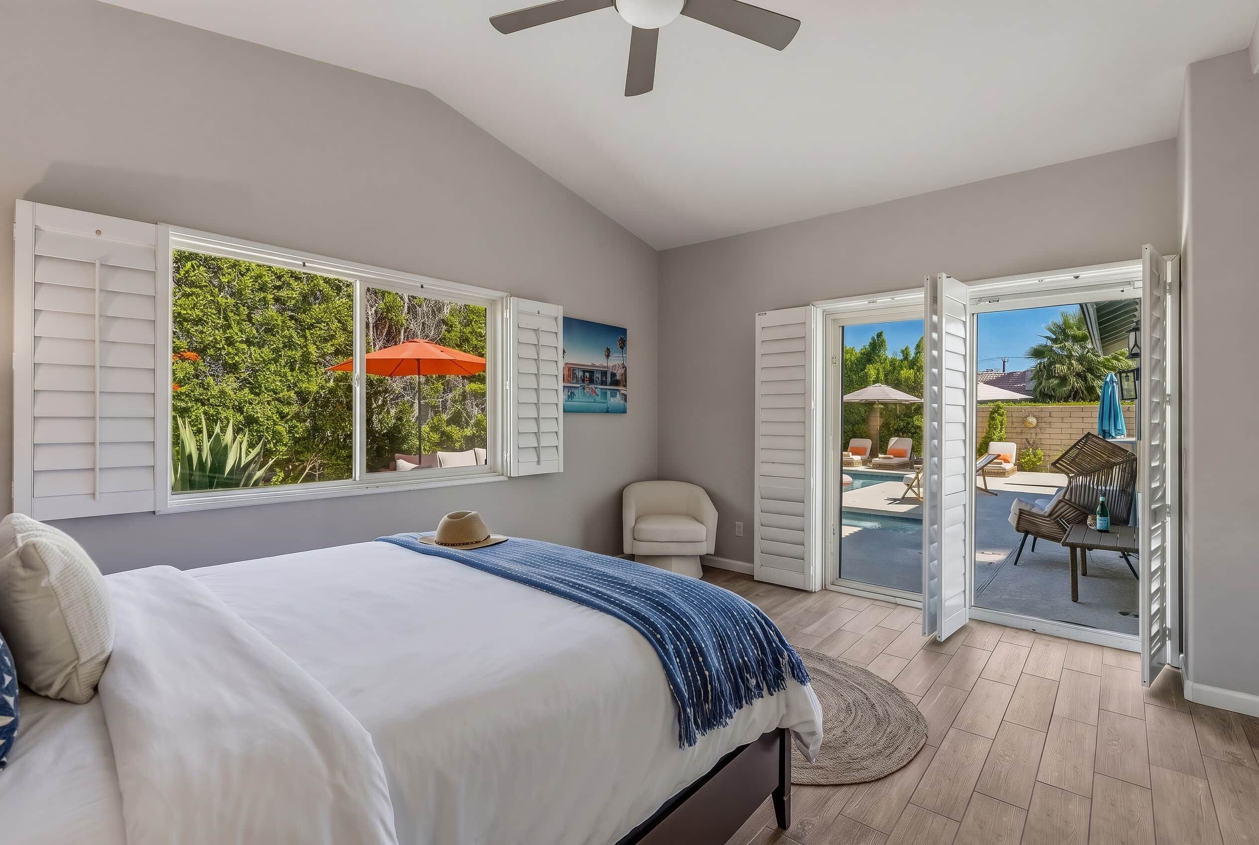 A bedroom with a bed, a ceiling fan, and a view of an outdoor swimming pool area.