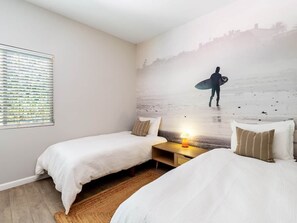A room with two beds, a nightstand with a lamp, and a mural of a surfer on a beach. - Cool Pool/Spa Retreat near Shops & Surf Club (Palm Springs)
