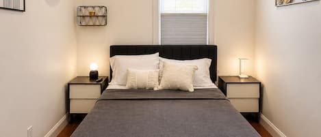 A bedroom with a bed, two bedside tables, a window, and wall decorations.