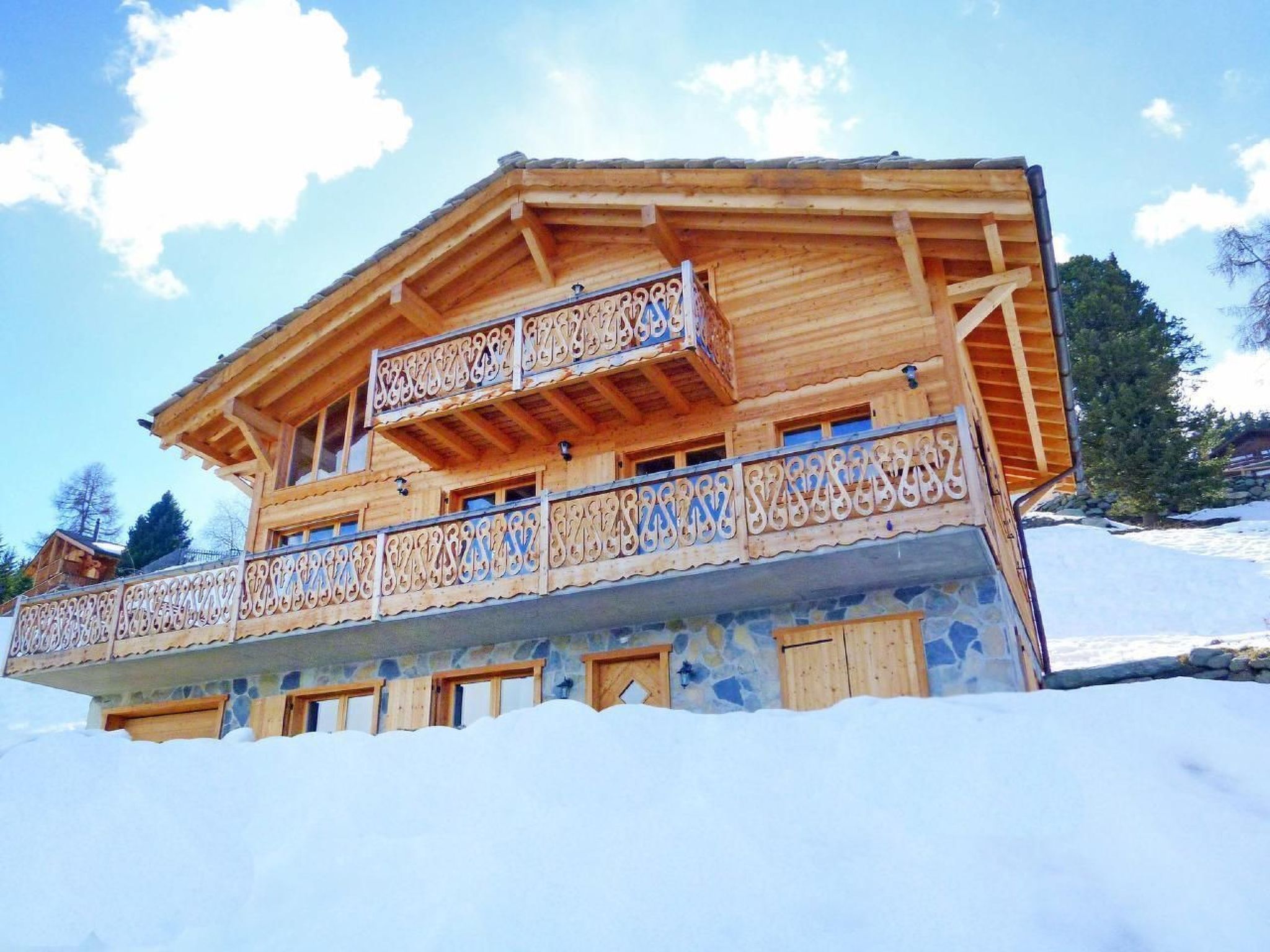 A wooden chalet with a balcony, stone walls, and a snowy landscape.