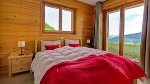 Une chambre à coucher aux murs lambrissés, avec un lit, deux tables de chevet et de grandes fenêtres donnant sur l’extérieur.