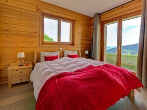 A wooden-paneled bedroom with a bed, two bedside tables, and large windows offering a view of the outdoors. - Perle des Collons by Interhome (Thyon-Les Collons)