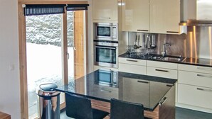 Eine moderne Küche mit einer zentralen Kochinsel, zwei Barhocker, Edelstahlgeräten und Blick auf eine verschneite Landschaft.
