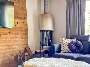 A modern living room with a wood-paneled wall, a large fireplace, a sofa with patterned cushions, and a fluffy white rug. - Chalet Marguerite by Interhome (Thyon-Les Collons)