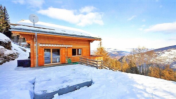 Eine Holzhütte mit Satellitenschüssel, einer Holzterrasse und verschneiter Landschaft.