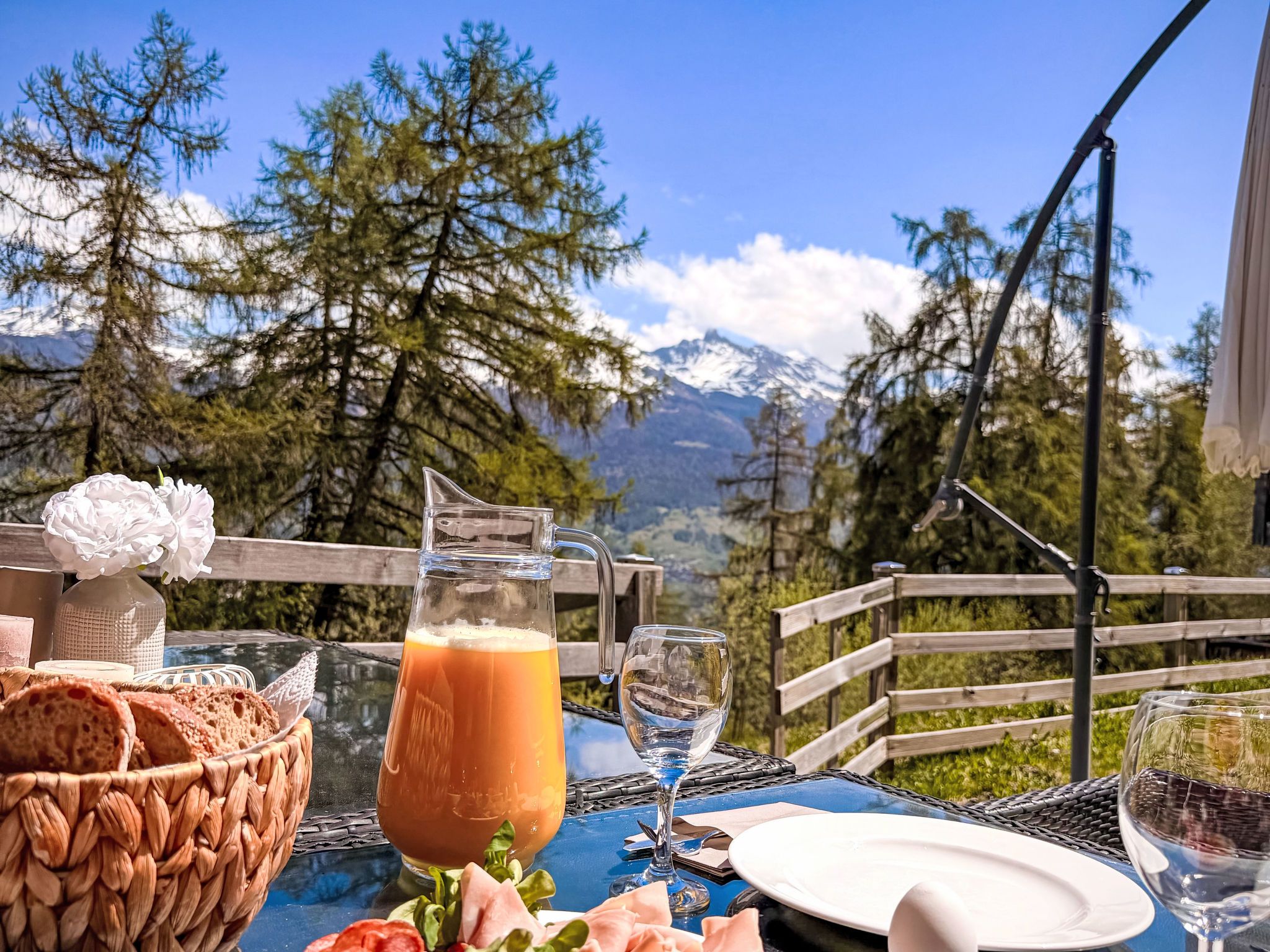 Une table dressée à l’extérieur, avec un verre de jus d’orange, du pain et un panier de fleurs.