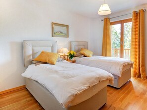 Ein Doppelzimmer mit zwei Betten, einem Nachttisch mit Lampe, einem gerahmten Bild an der Wand und einem Fenster mit Vorhängen.