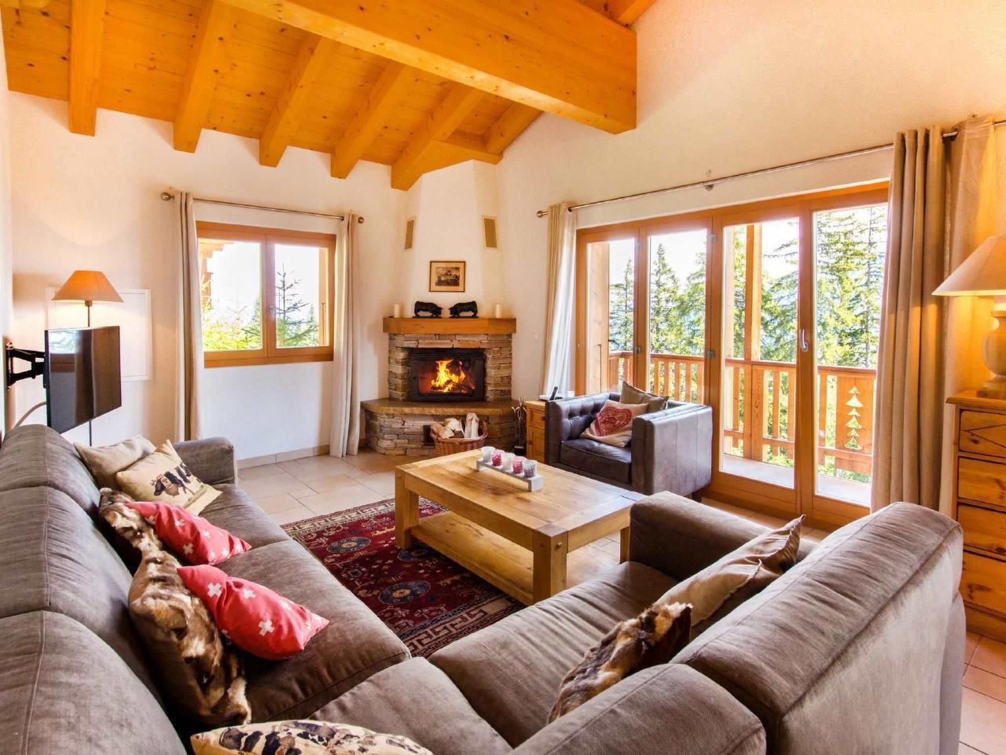 A cozy living room with a fireplace, large windows, and a wooden ceiling.