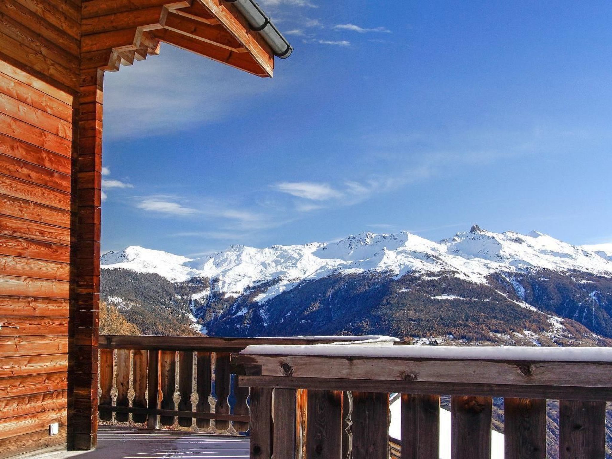 Un balcon en bois offrant une vue sur des montagnes enneigées.
