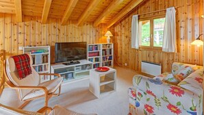 Ein gemütliches Blockhaus-Interieur mit Holzwänden, einem Fernseher, Bücherregalen, einer Couch und einem Sessel.