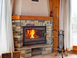 Une cheminée en pierre avec un foyer apparent, une cheminée en bois et un récupérateur de cendres en métal.