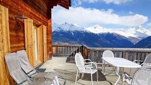 Eine Holzhütte mit Balkon, Sitzgelegenheit im Freien und Blick auf die Berge.