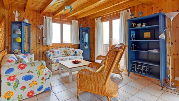 Ein Holzblockhaus-Innenraum mit einer Couch, Stühlen, einem Tisch und einem Bücherregal.