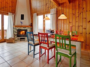 L’intérieur chaleureux d’un chalet avec une cheminée en pierre, des murs en bois et un coin repas agrémenté de chaises colorées.