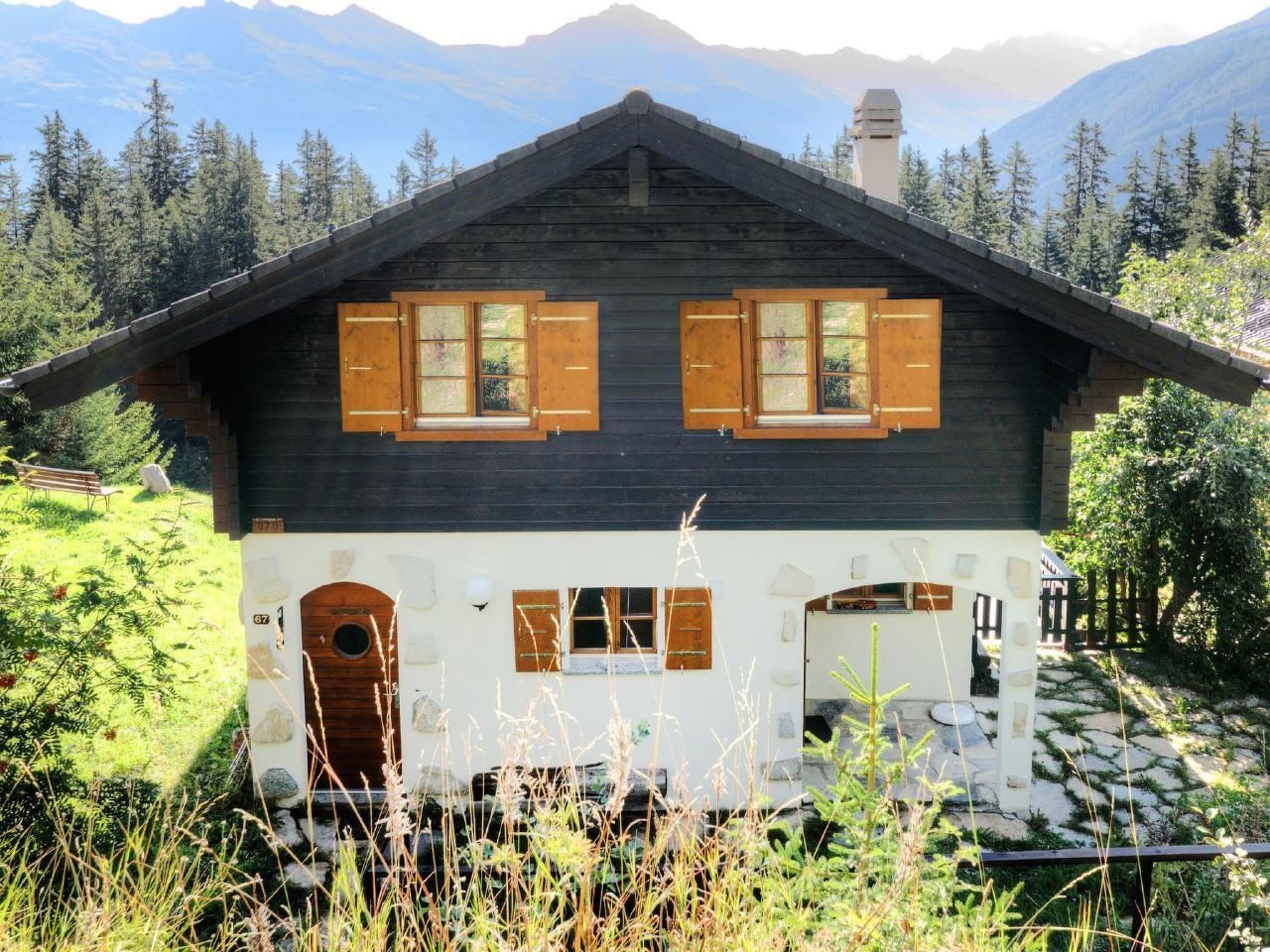 Une cabane en bois avec un toit sombre, deux fenêtres dotées de volets en bois, une porte d’entrée et un chemin de pierre menant à la cabane.