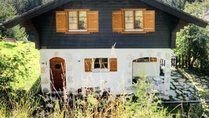 A wooden cabin with a dark roof, two windows with wooden shutters, a front door, and a stone pathway leading to it. - Chalet Altitude 1900 by Interhome (Thyon-Les Collons)