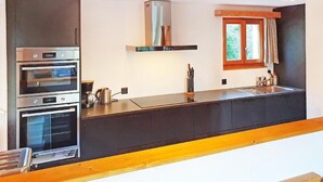 A modern kitchen with built-in ovens, a coffee maker, and a window with curtains. - Chalet Altitude 1900 by Interhome (Thyon-Les Collons)
