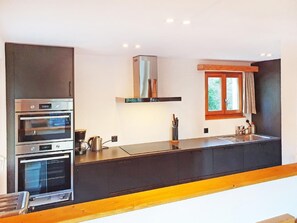 A modern kitchen with built-in ovens, a coffee maker, and a window with curtains.