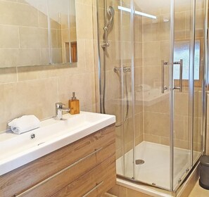 Ein modernes Badezimmer mit Duschkabine aus Glas, Holzwaschbecken und einem großen Spiegel.