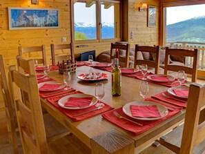 Mesa de madera dispuesta para seis personas, con servilletas rojas, copas de vino y una botella.
