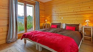 A wooden cabin bedroom with a bed, two bedside tables, and a window with curtains. - Chalet Bryher by Interhome (Thyon-Les Collons)