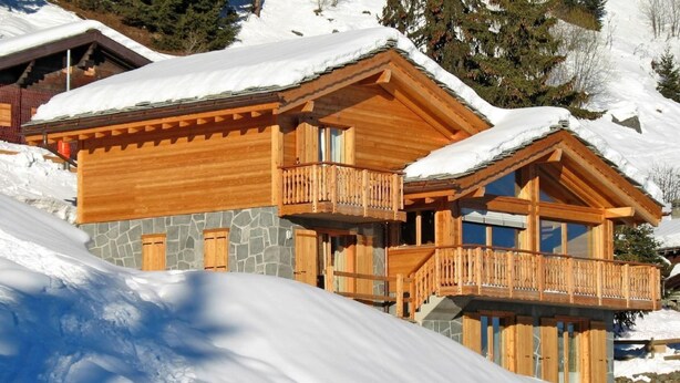 A wooden chalet with a stone facade, wooden balconies, and a snow-covered roof. - Chalet Bryher by Interhome (Thyon-Les Collons)