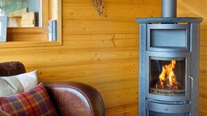 A cozy room with a leather sofa, a fireplace with visible flames, and wooden panel walls. - Chalet Bryher by Interhome (Thyon-Les Collons)