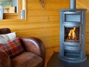 A cozy room with a leather sofa, a fireplace with visible flames, and wooden panel walls. - Chalet Bryher by Interhome (Thyon-Les Collons)