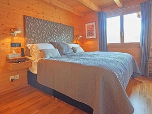 Ein Schlafzimmer mit Holzwand, einem Bett, Nachttischlampen, einem Beistelltisch und einem Fenster mit Vorhängen.