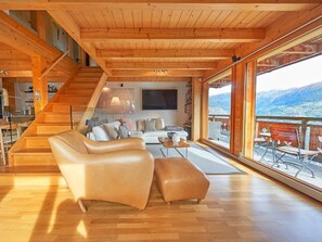 Ein großzügiger Wohnbereich mit einer Holztreppe, einem Sofa, einem Couchtisch und einem großen Fenster mit Blick auf die Berge.