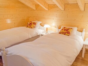 Una habitación con dos camas individuales, paredes de madera, un cabecero blanco y una lámpara de noche.