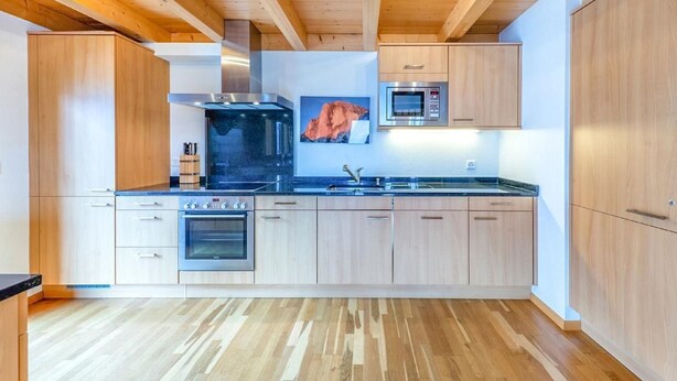 A modern kitchen with wooden cabinets, a stainless steel oven, a microwave, and a large black stove. - Chalet Greppon Blanc by Interhome (Hérémence)