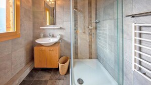 A modern bathroom with a glass shower enclosure, a wooden vanity with two sinks, and a white bathtub. - Chalet Greppon Blanc by Interhome (Hérémence)