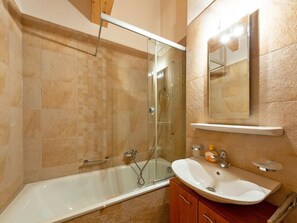 Un baño con bañera, ducha con mampara de vidrio, lavamanos y espejo.