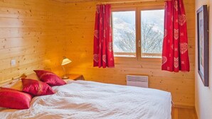 A wooden cabin bedroom with a bed, pillows, a lamp, and a window with curtains. - Chalet Greppon Blanc by Interhome (Hérémence)