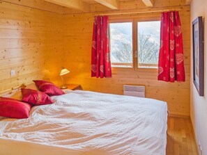 Ein Schlafzimmer einer Holzhütte mit einem Bett, Kissen, einer Lampe und einem Fenster mit Vorhängen.