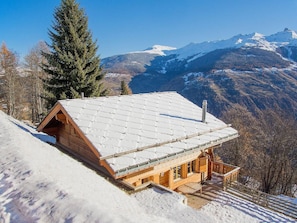 Eine Holzhütte mit geneigtem Dach, umgeben von schneebedeckten Bergen und einem klaren Himmel.