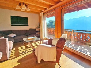 A cozy living room with a sofa, armchair, and coffee table, a balcony with a view of mountains, and wooden beams on the ceiling. - Chalet Mountain Star by Interhome (Hérémence)