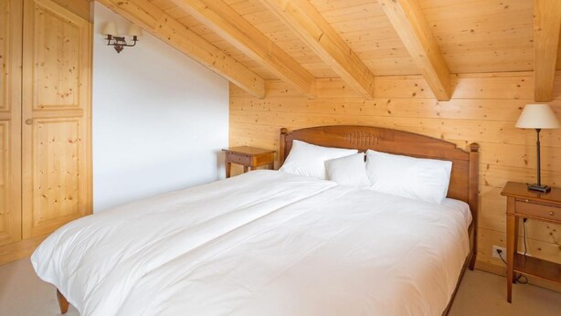 Un dormitorio con paneles de madera, una cama, mesitas de noche y una lámpara de pared.