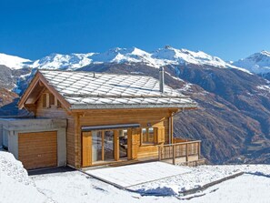 A wooden cabin with a balcony, a garage, and a view of snow-covered mountains. - Chalet Falcons Nest by Interhome (Hérémence)