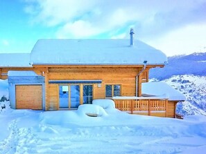 Uma cabana de madeira com entrada coberta e um deck, rodeada por neve.