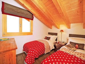 A room with two beds, a window with a red valance, a wooden ceiling, and a nightstand with a lamp. - Chalet Falcons Nest by Interhome (Hérémence)