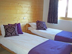 Two single beds with headboards against a wooden wall, a window with curtains, and a light switch on the wall. - Chalet Ourson Blanc by Interhome (Hérémence)