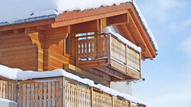 Een houten chalet met balkon en schoorsteen, omgeven door sneeuw.