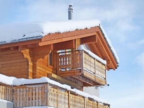 Eine Holzhütte mit Balkon und Schornstein, umgeben von Schnee.