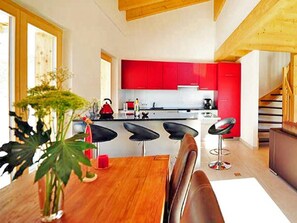 A modern kitchen with red cabinets, a wooden dining table, and black bar stools. - Chalet Ourson Blanc by Interhome (Hérémence)