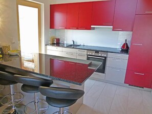 A modern kitchen with red cabinets, a stainless steel countertop, and a bar area with stools. - Chalet Ourson Blanc by Interhome (Hérémence)