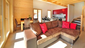 Een moderne woonkamer met een ruime hoekbank, een eethoek en een keuken met rode keukenkastjes.